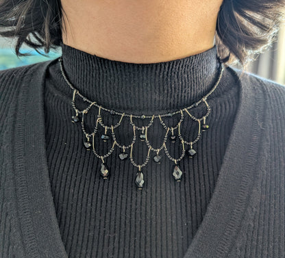 Person wearing a black turtleneck sweater with a decorative black bead choker necklace.
