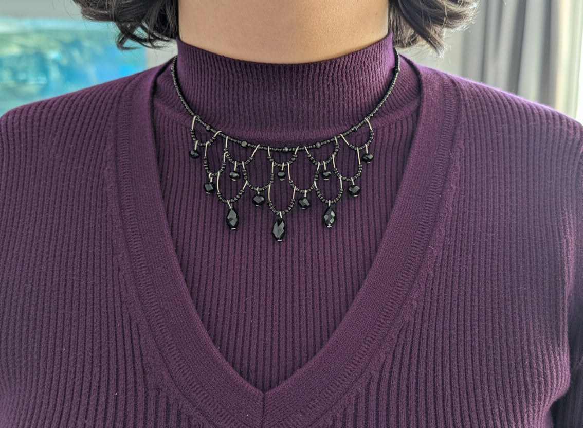 Person wearing a purple sweater and a decorative necklace with black beads.