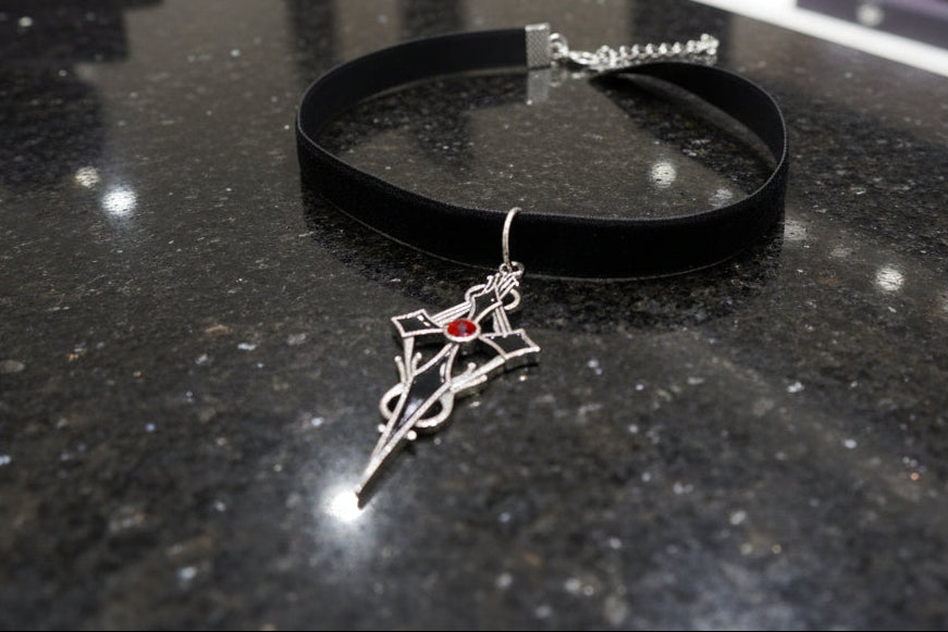 Black choker with a silver and red pendant on a dark surface