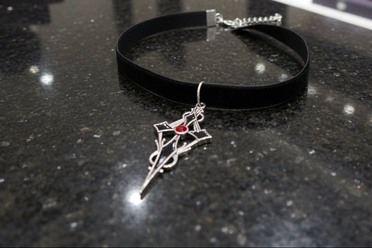 Black choker with a silver and red pendant on a dark surface