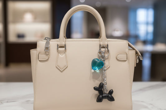 "Handmade black glitter balloon dog charm with teal heart on a cream designer handbag."