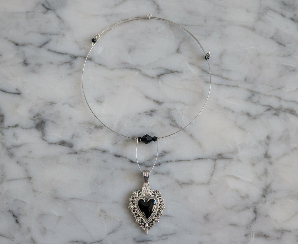 This elegant memory wire choker combines timeless style with modern sophistication. Featuring a striking black stainless steel heart pendant accented with lustrous black beads, it adjusts perfectly to fit neck sizes 4 to 4.5 inches. The durable .025" wire construction ensures lasting wear without losing its shape, while the lightweight design at just 0.28 oz makes it comfortable for all-day elegance. Whether layered with other pieces or worn solo, this versatile choker adds an instant touch of charm to any 