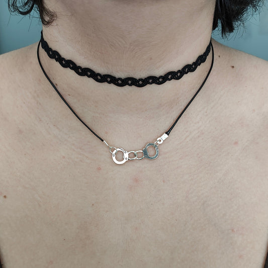 Add a touch of playful edge to your outfit with our Choker Necklace featuring black lace ribbon, a sturdy polyester strand, and a fun handcuff charm. Perfect for adding some cheeky charm to your look!