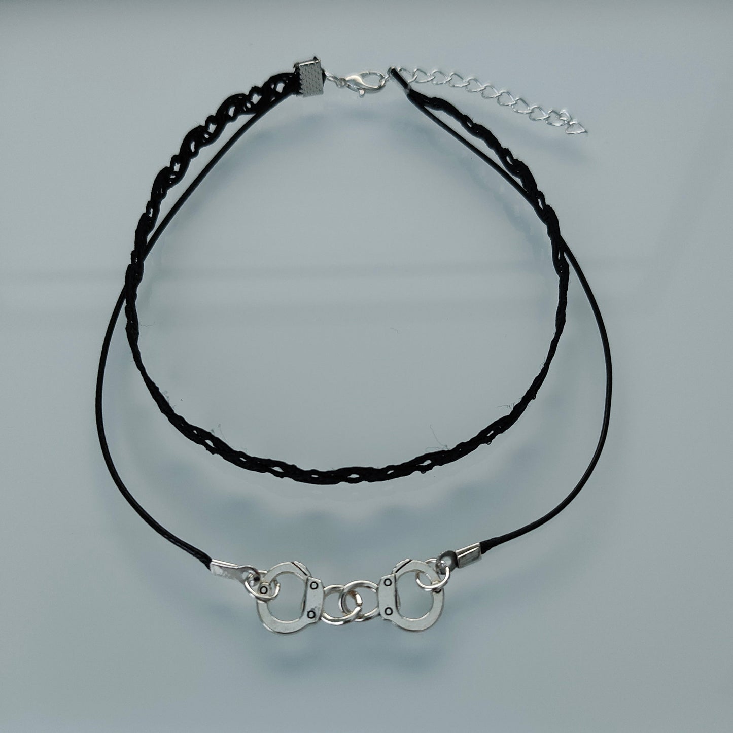 Add a touch of playful edge to your outfit with our Choker Necklace featuring black lace ribbon, a sturdy polyester strand, and a fun handcuff charm. Perfect for adding some cheeky charm to your look!