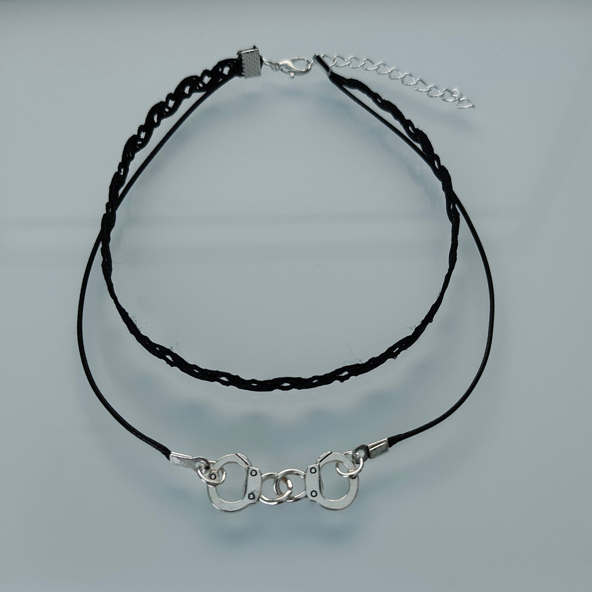 Add a touch of playful edge to your outfit with our Choker Necklace featuring black lace ribbon, a sturdy polyester strand, and a fun handcuff charm. Perfect for adding some cheeky charm to your look!