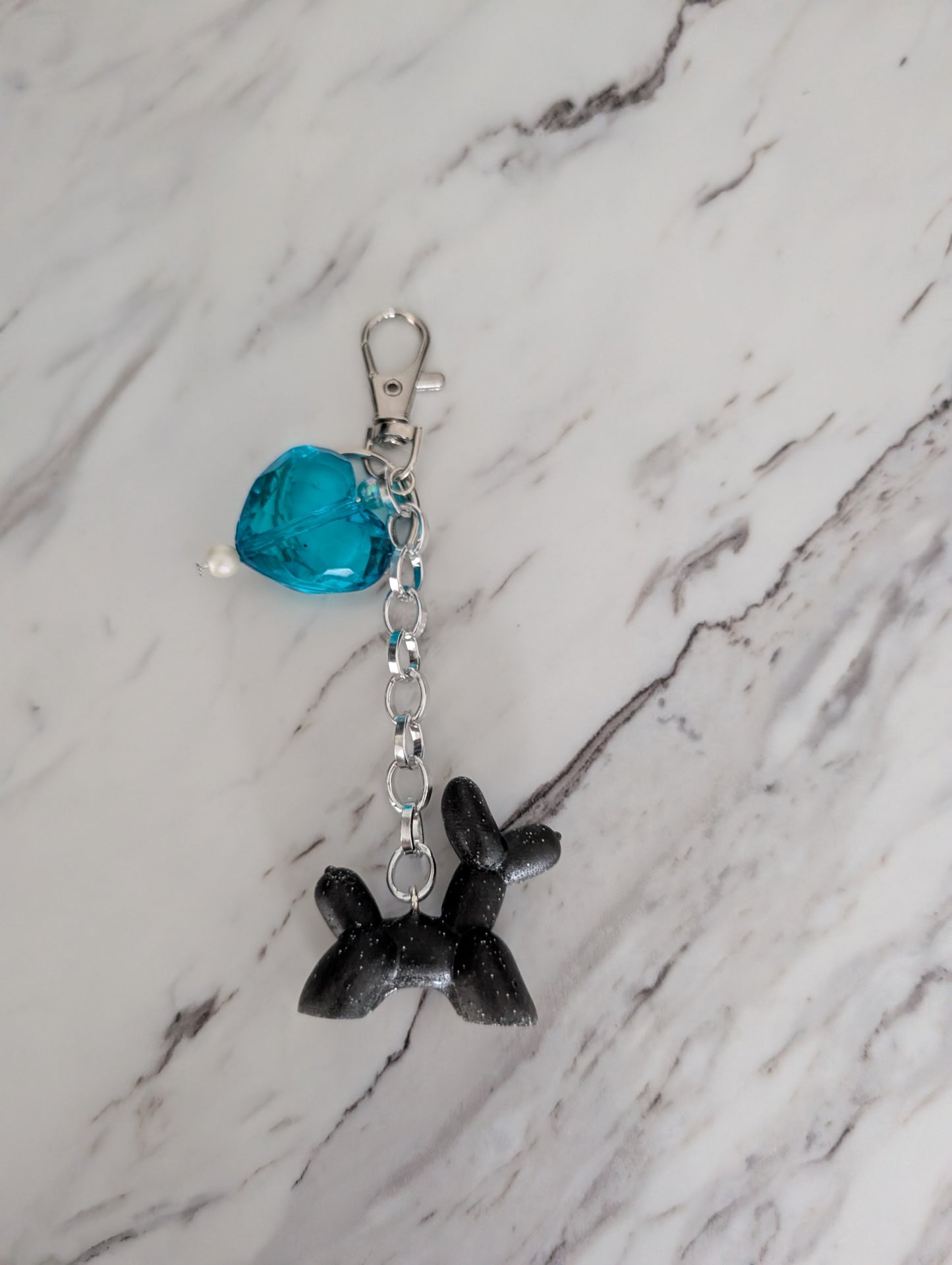 Black dog-shaped keychain with a blue crystal on a marble surface