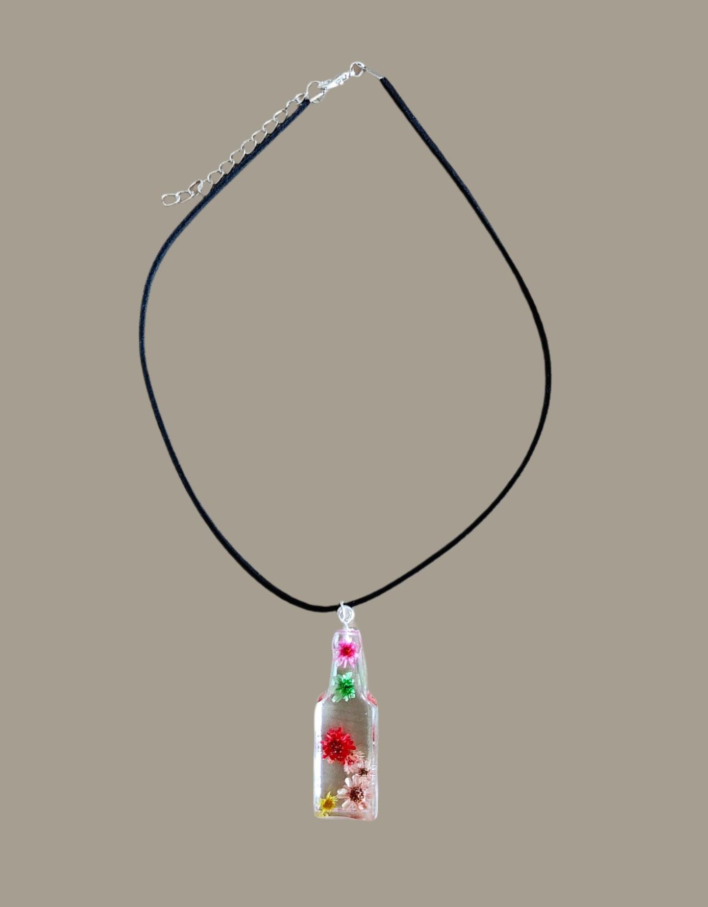 Wear our stunning 15.5 inch black suede cord necklace with a unique resin bottle pendant adorned with delicate flowers. Elevate your style and add a touch of whimsy to any outfit. Perfect for any occasion, this necklace is a must-have for any fashion-forward individual.