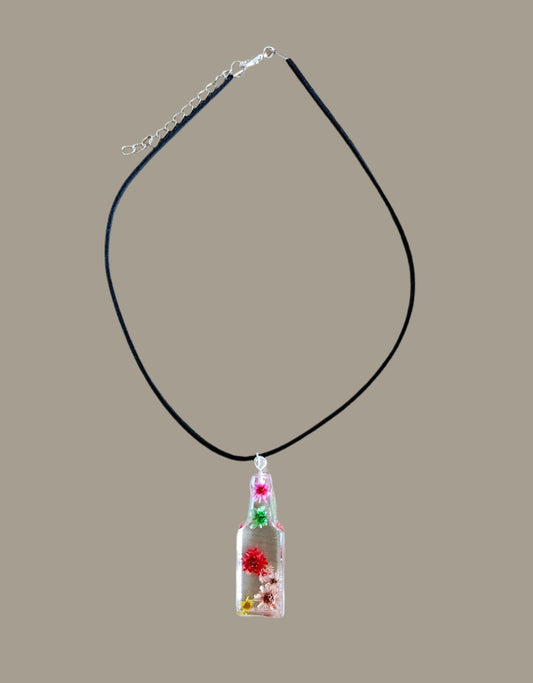 Wear our stunning 15.5 inch black suede cord necklace with a unique resin bottle pendant adorned with delicate flowers. Elevate your style and add a touch of whimsy to any outfit. Perfect for any occasion, this necklace is a must-have for any fashion-forward individual.
