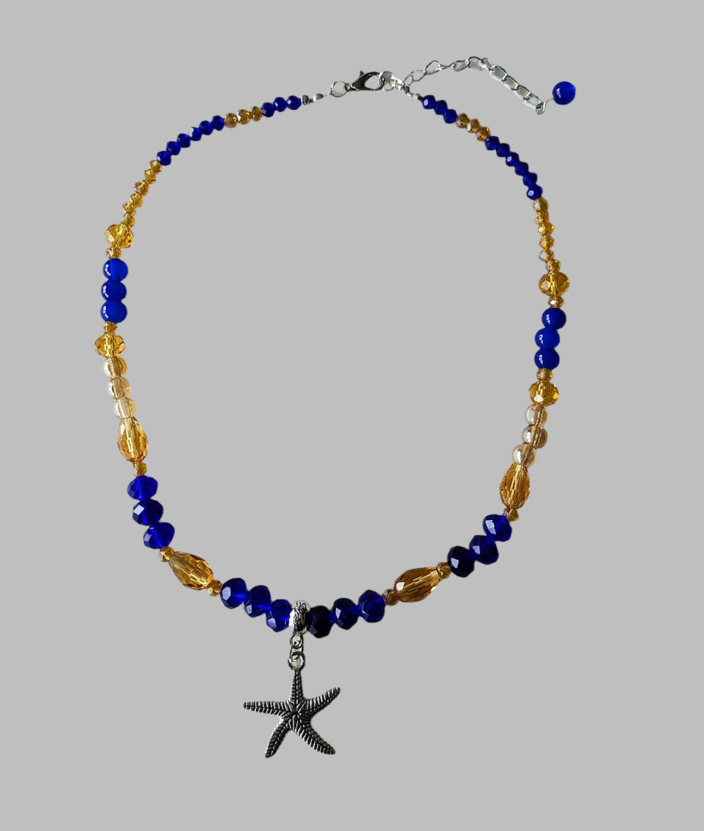 Add a touch of the ocean to your outfit with our Silver Starfish Necklace. Featuring a delicate silver starfish charm adorned with blue and gold crystal and glass beads, this necklace is perfect for any occasion. Choose between 16 and 18 inches for the perfect fit, and enjoy its lightweight design at only 0.72 oz.

Necklace - Silver starfish charm with blue and gold crystal and glass beads