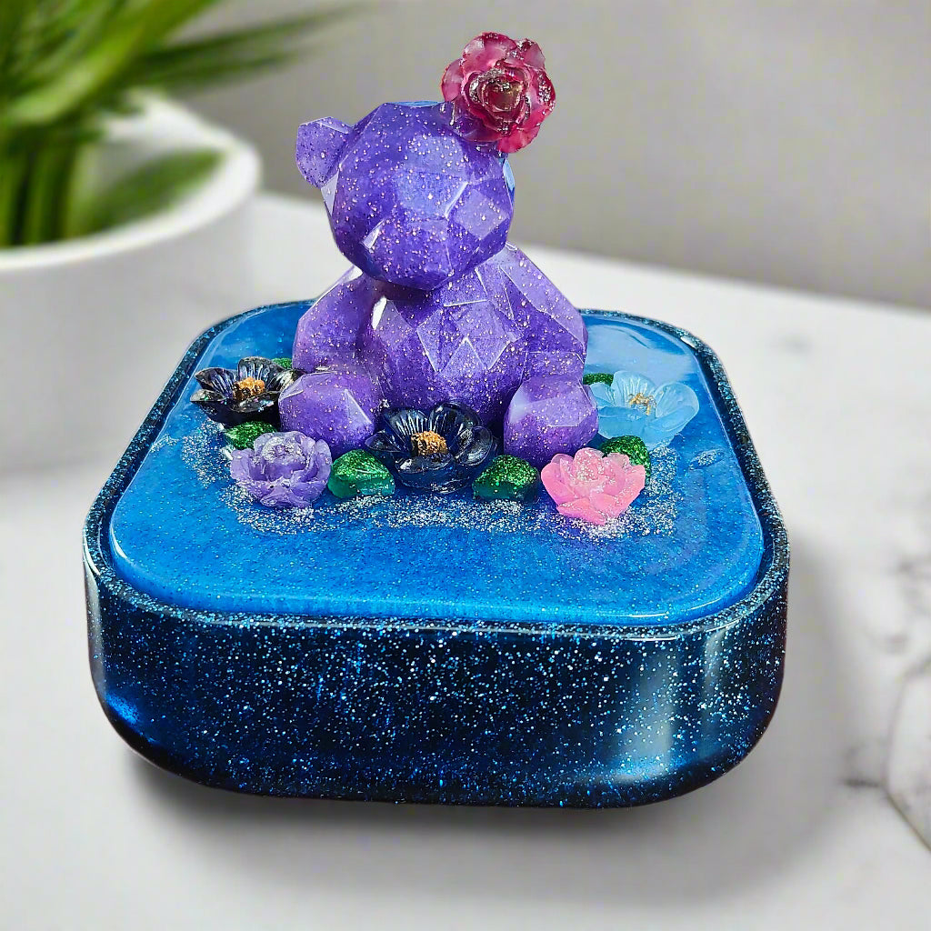 Elevate your jewelry storage with our Knickknack - Large resin square box! Featuring a charming bear and flowers lid, it adds a whimsical touch to any room. Boasting ample space for your precious items, it's the perfect blend of function and beauty. Upgrade to this stunning jewelry box today!