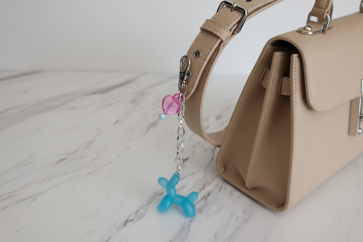 Blue balloon dog keychain with pink heart charm on a marble surface