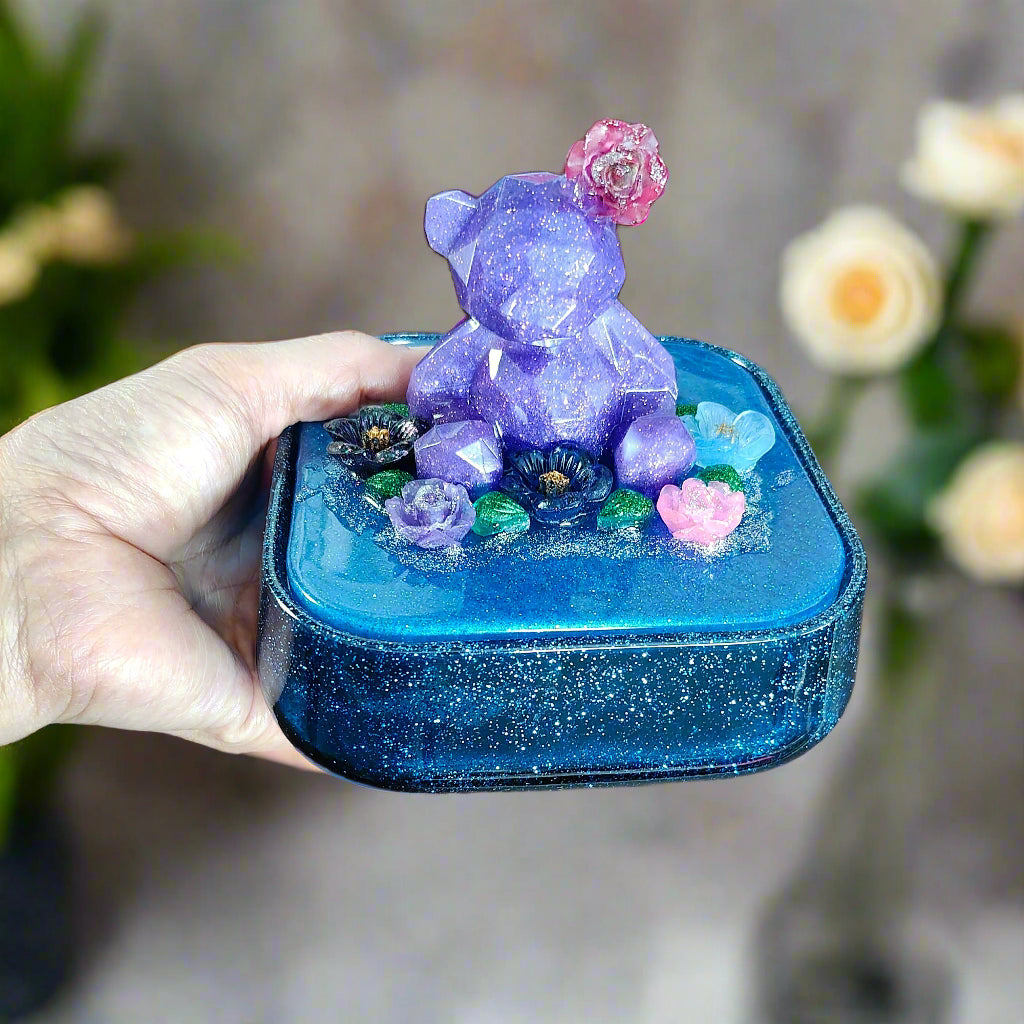 Elevate your jewelry storage with our Knickknack - Large resin square box! Featuring a charming bear and flowers lid, it adds a whimsical touch to any room. Boasting ample space for your precious items, it's the perfect blend of function and beauty. Upgrade to this stunning jewelry box today!