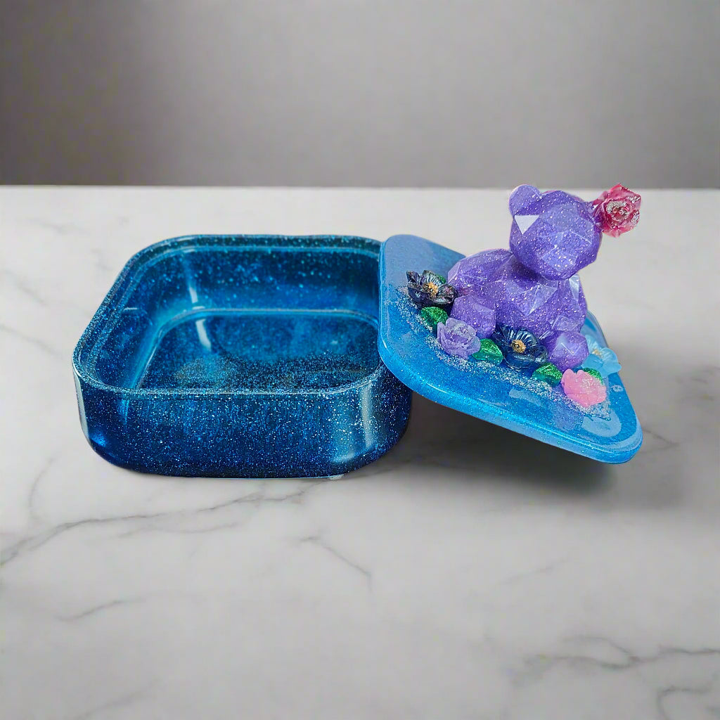 Elevate your jewelry storage with our Knickknack - Large resin square box! Featuring a charming bear and flowers lid, it adds a whimsical touch to any room. Boasting ample space for your precious items, it's the perfect blend of function and beauty. Upgrade to this stunning jewelry box today!