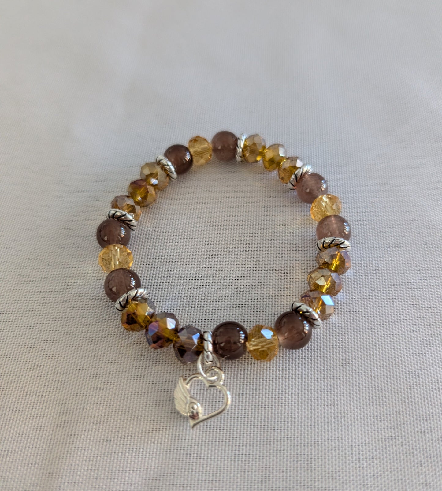 Express your heart with this warm and radiant elastic bracelet that combines rich brown and gold tones with timeless sentiment. Featuring 8mm brown and gold beads interspersed with sparkling crystal and glass accents, silver spacers, and a delicate silver heart charm, this piece speaks to both style and emotion. The elastic band stretches effortlessly to fit any wrist, requiring no clasps or adjustments—just slip it on and go. Weighing a comfortable 0.60 oz, it's substantial enough to feel quality yet light