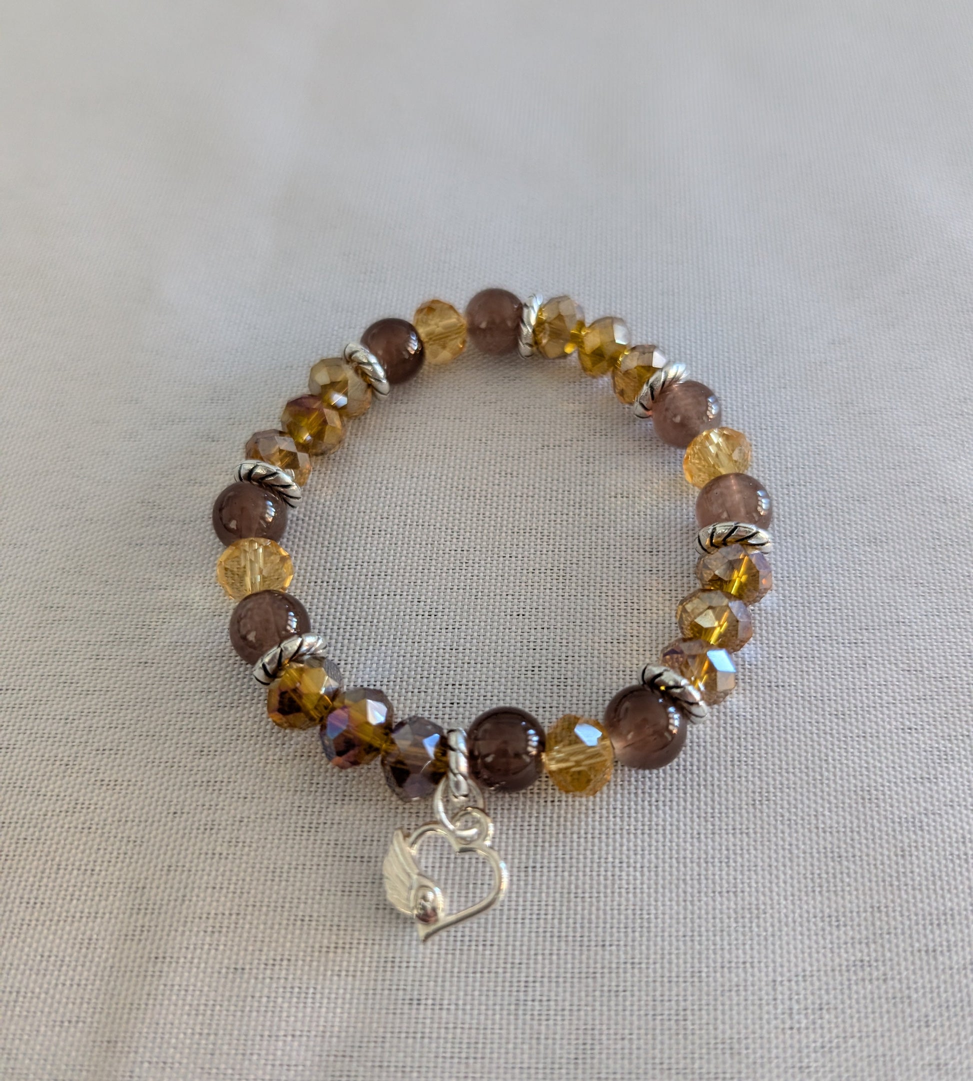 Express your heart with this warm and radiant elastic bracelet that combines rich brown and gold tones with timeless sentiment. Featuring 8mm brown and gold beads interspersed with sparkling crystal and glass accents, silver spacers, and a delicate silver heart charm, this piece speaks to both style and emotion. The elastic band stretches effortlessly to fit any wrist, requiring no clasps or adjustments—just slip it on and go. Weighing a comfortable 0.60 oz, it's substantial enough to feel quality yet light