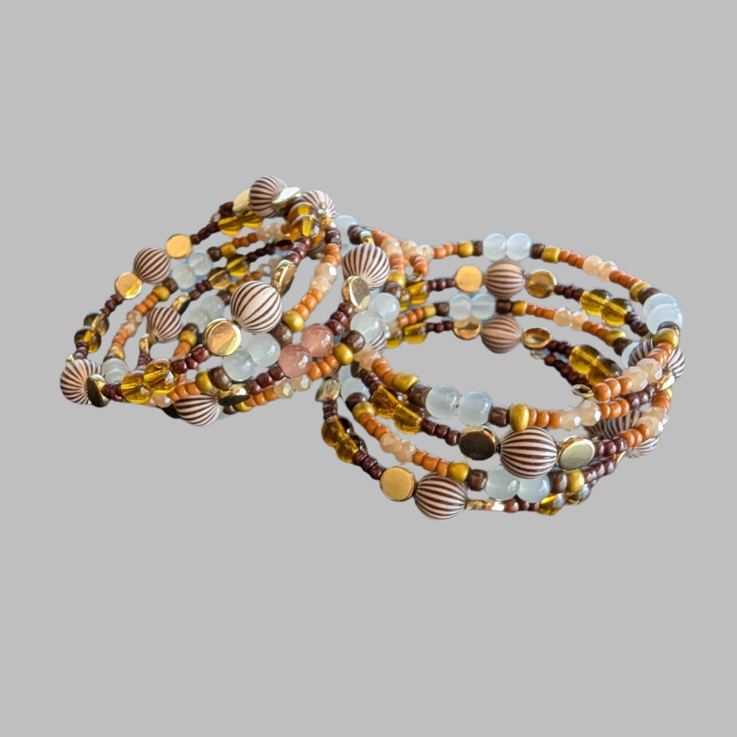 This elegant memory wire bracelet features four coils adorned with brown, white, and tan beads, complemented by gold, brown, and tan spacer beads. Its versatile color palette pairs effortlessly with any outfit, while the flexible design ensures a comfortable fit for all wrist sizes. Add a touch of sophistication and warmth to your look with this stylish accessory.