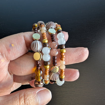 This elegant memory wire bracelet features four coils adorned with brown, white, and tan beads, complemented by gold, brown, and tan spacer beads. Its versatile color palette pairs effortlessly with any outfit, while the flexible design ensures a comfortable fit for all wrist sizes. Add a touch of sophistication and warmth to your look with this stylish accessory.