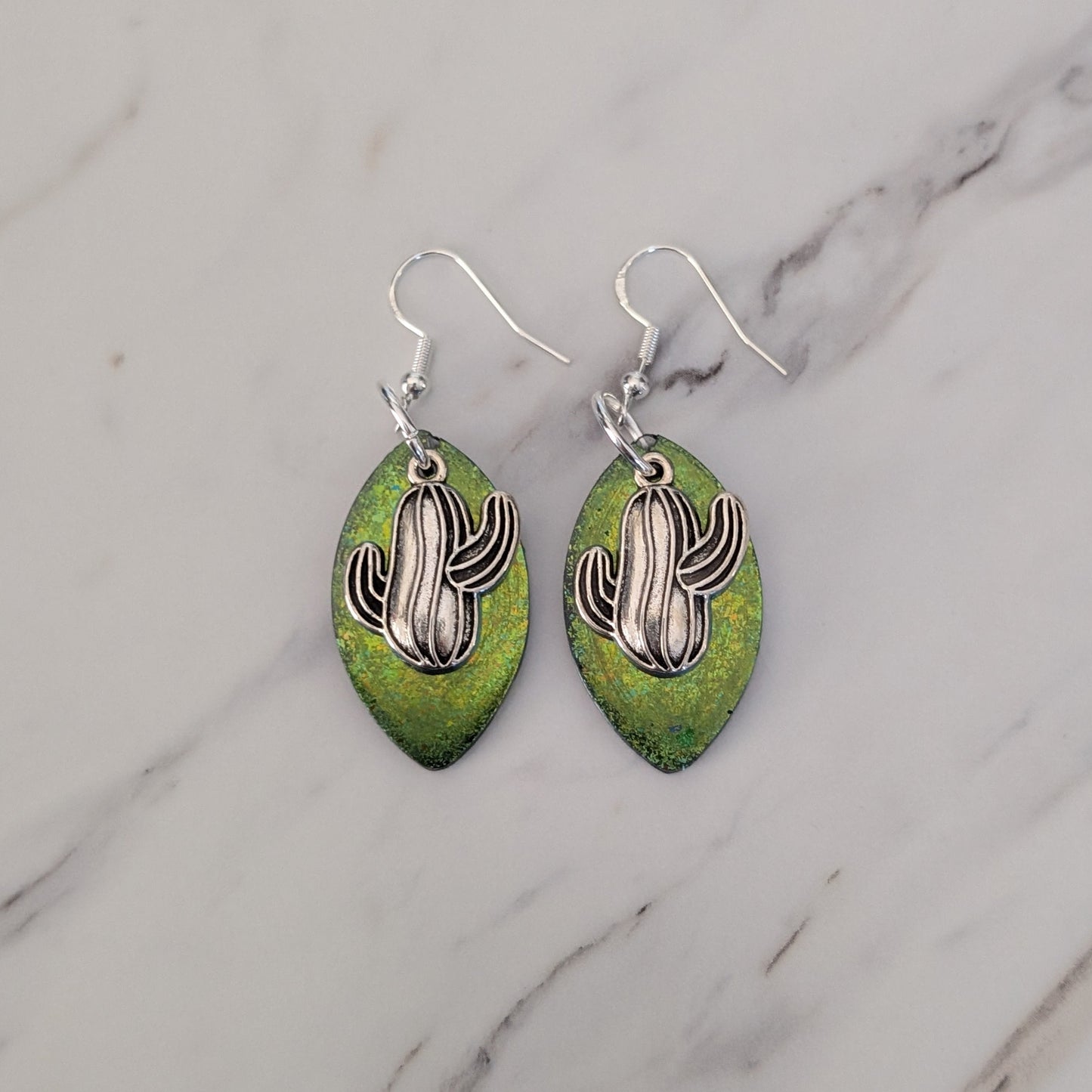 Pair of earrings with cactus design on green leaves against a marble background