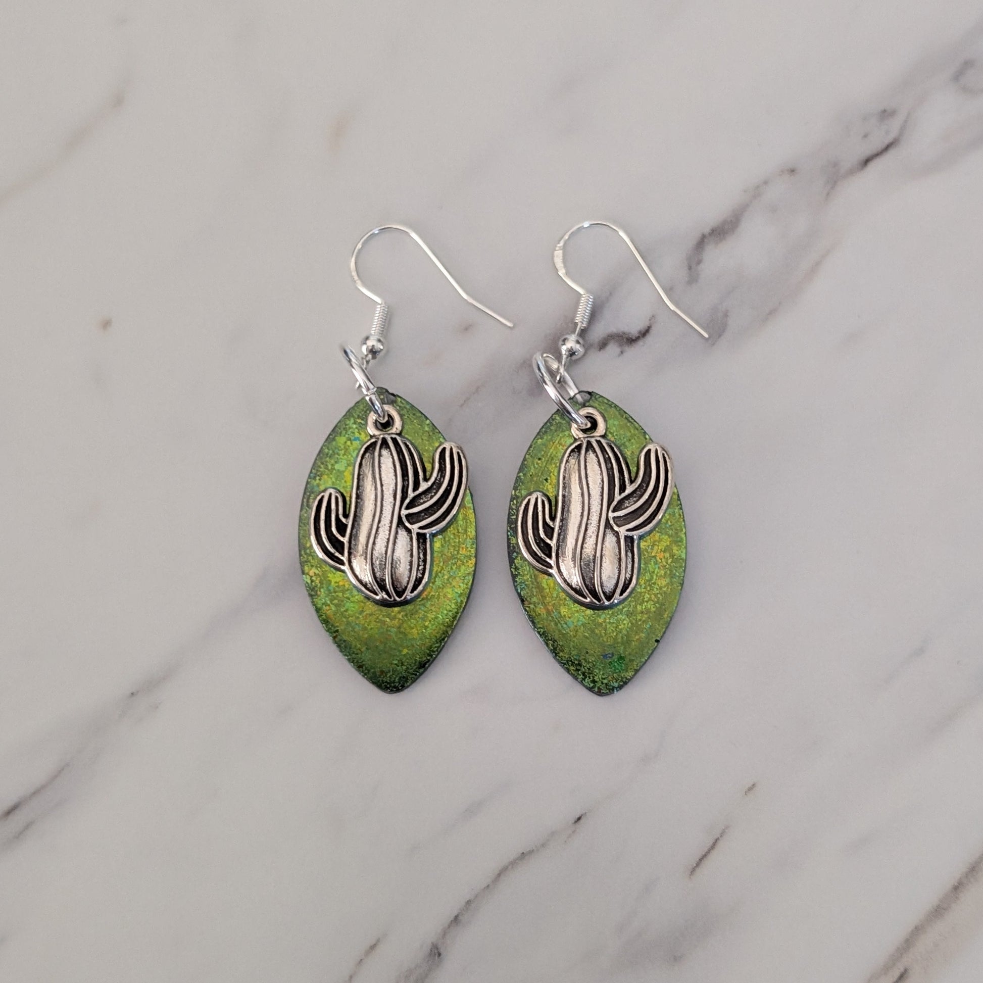 Pair of earrings with cactus design on green leaves against a marble background