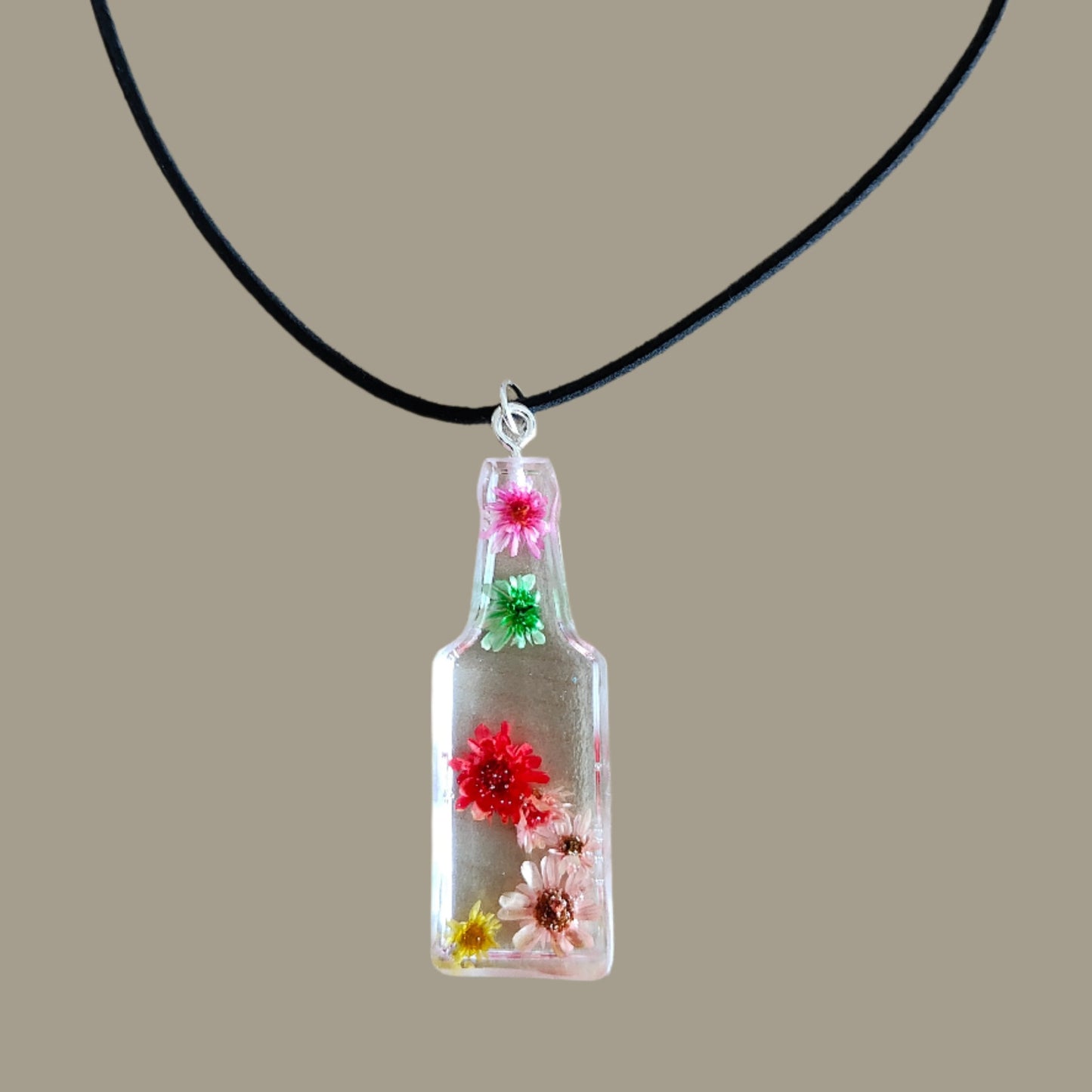 Wear our stunning 15.5 inch black suede cord necklace with a unique resin bottle pendant adorned with delicate flowers. Elevate your style and add a touch of whimsy to any outfit. Perfect for any occasion, this necklace is a must-have for any fashion-forward individual.