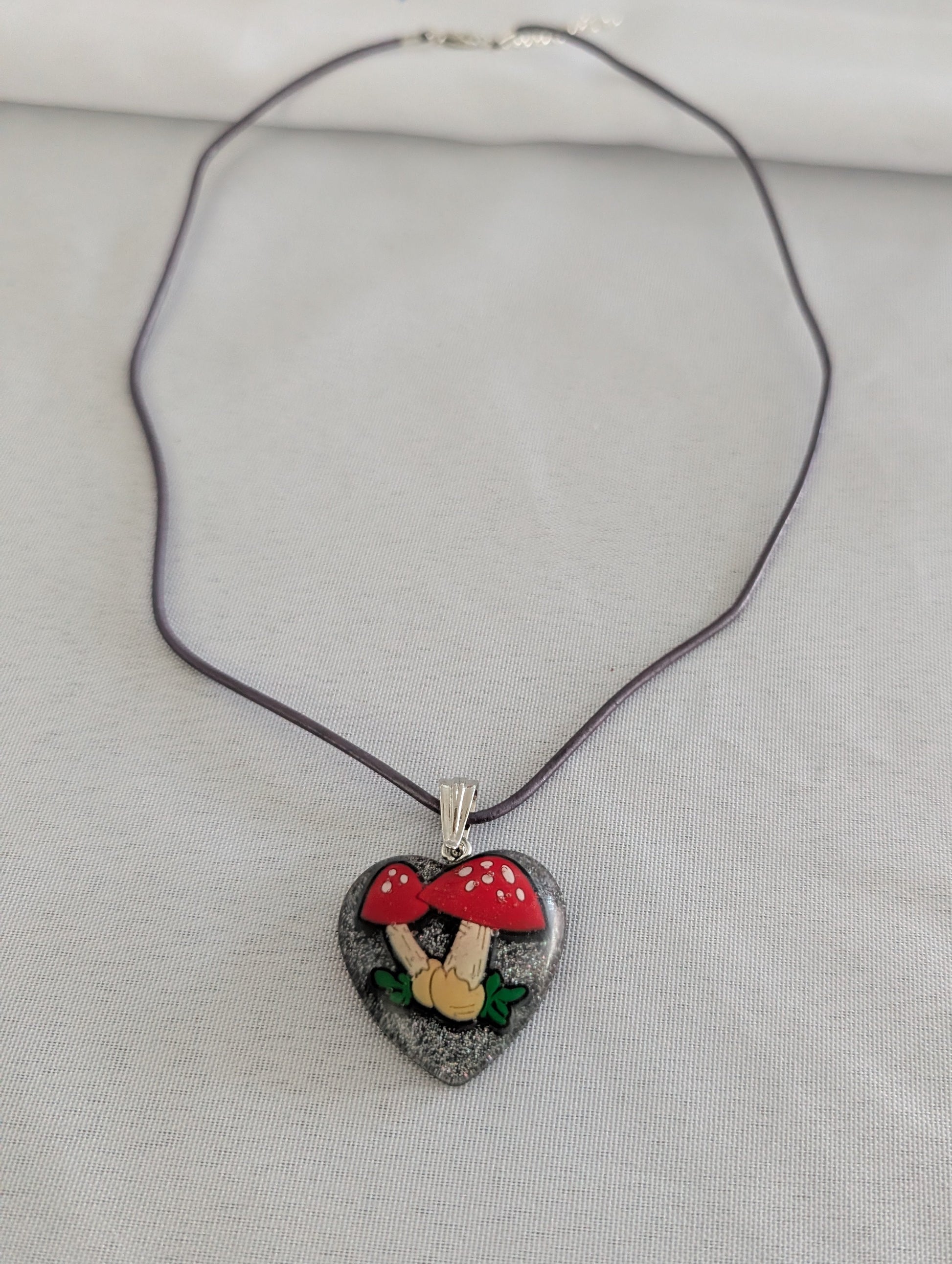Heart-shaped pendant with a mushroom design on a purple cord against a light gray background