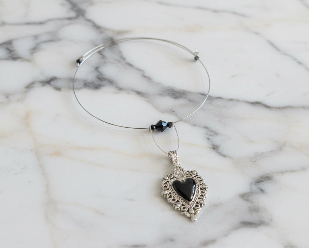 This elegant memory wire choker combines timeless style with modern sophistication. Featuring a striking black stainless steel heart pendant accented with lustrous black beads, it adjusts perfectly to fit neck sizes 4 to 4.5 inches. The durable .025" wire construction ensures lasting wear without losing its shape, while the lightweight design at just 0.28 oz makes it comfortable for all-day elegance. Whether layered with other pieces or worn solo, this versatile choker adds an instant touch of charm to any 