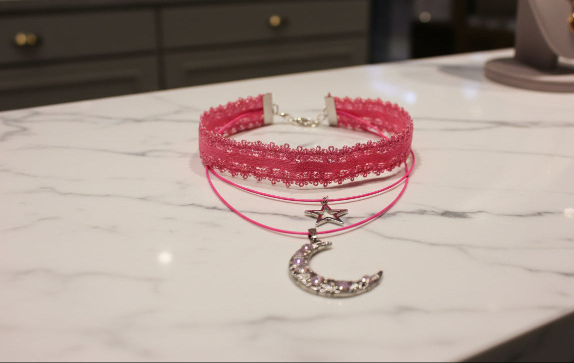 Transform any outfit into a stellar ensemble with this playful Necklace-Choker! Featuring an elastic lace ribbon, two polyester strands, and a crystal-studded silver moon and star charm, this necklace adds a touch of whimsy to your look. Plus, with a 2 inch extension chain, it's perfect for any neckline.
