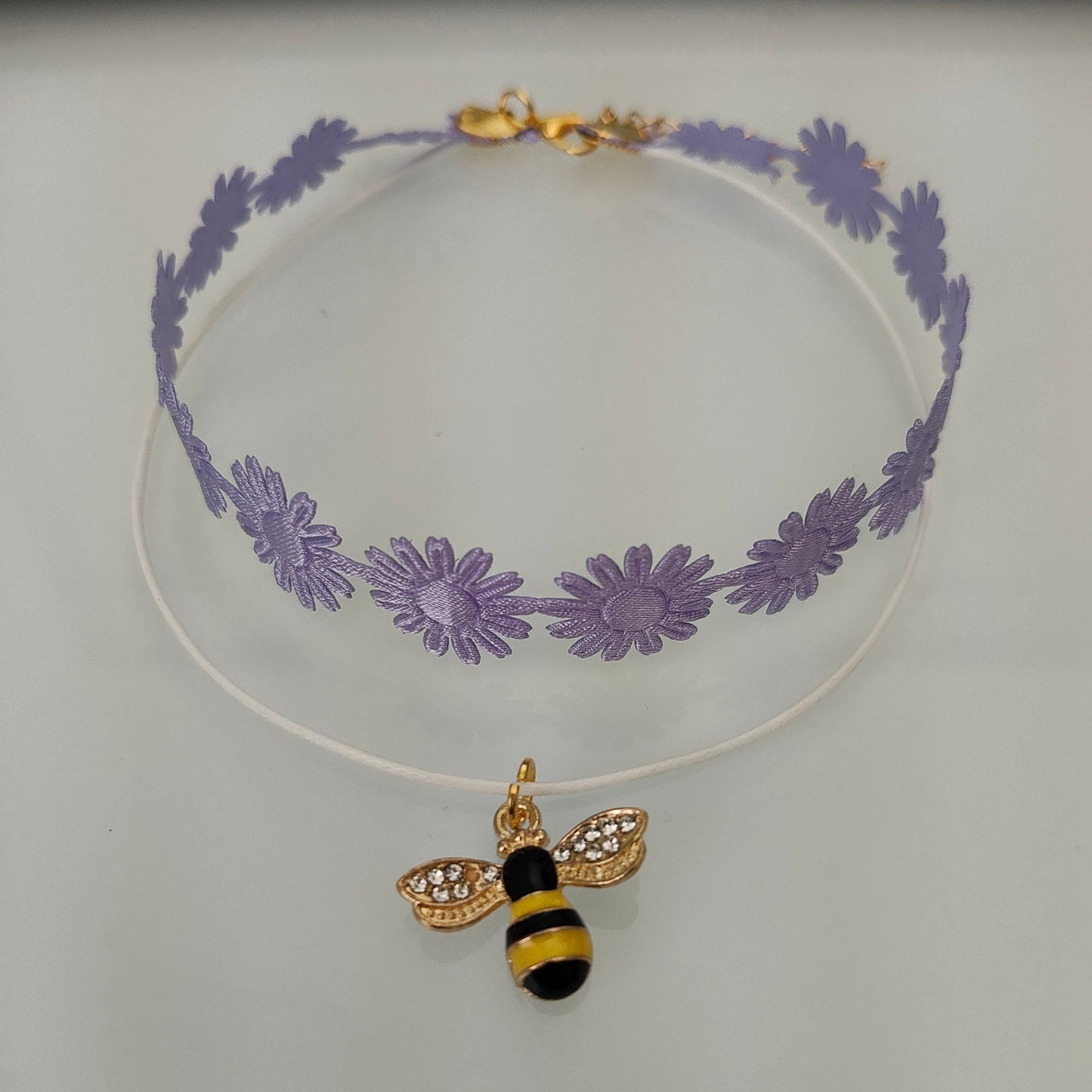 Get ready to make a buzz with this playful purple daisy choker! Featuring a charming bee charm and a trendy ribbon design, this necklace adds a touch of fun to any outfit. And with its durable polyester strand, you can rock this quirky accessory for any occasion.