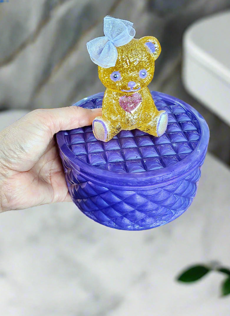 This adorable hand-crafted resin trinket box brings a touch of whimsy to your space! Featuring a charming teddy bear perched on top, it's the perfect home for jewelry, keepsakes, or small treasures. Measuring 5" x 5" x 5" with a 2" deep dish, this compact beauty combines functionality with personality. Crafted from smooth, durable epoxy resin that feels like glass, it's built to last while adding a playful accent to any dresser or shelf. At just 13 oz, it's lightweight enough to move around but sturdy enoug