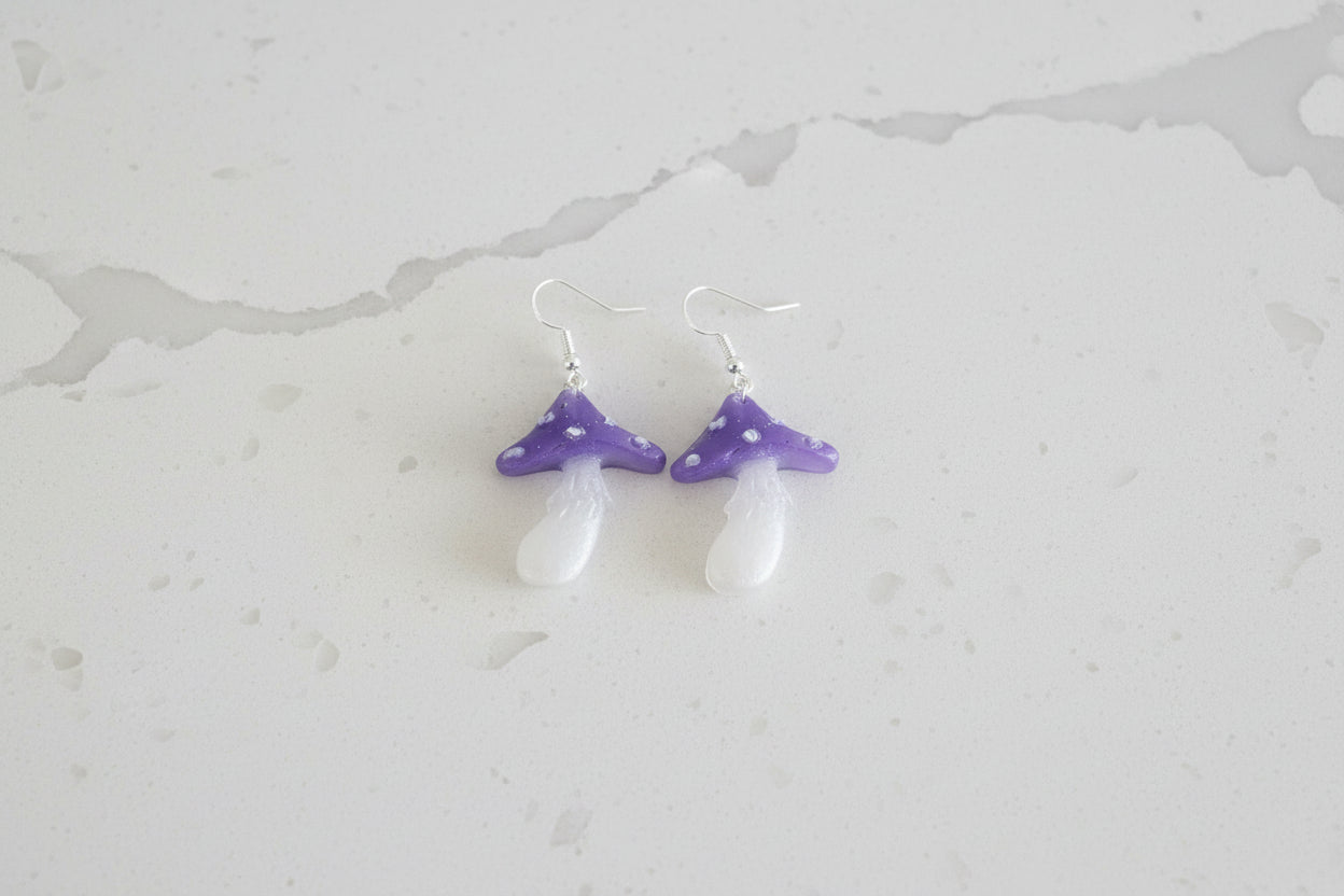 Pair of mushroom earrings with purple and white design on a light gray background
