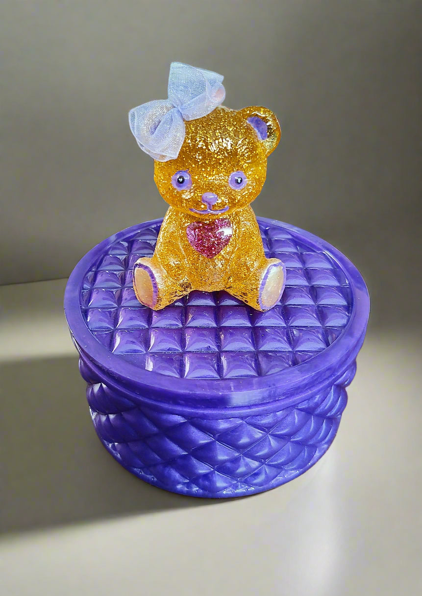 This adorable hand-crafted resin trinket box brings a touch of whimsy to your space! Featuring a charming teddy bear perched on top, it's the perfect home for jewelry, keepsakes, or small treasures. Measuring 5" x 5" x 5" with a 2" deep dish, this compact beauty combines functionality with personality. Crafted from smooth, durable epoxy resin that feels like glass, it's built to last while adding a playful accent to any dresser or shelf. At just 13 oz, it's lightweight enough to move around but sturdy enoug
