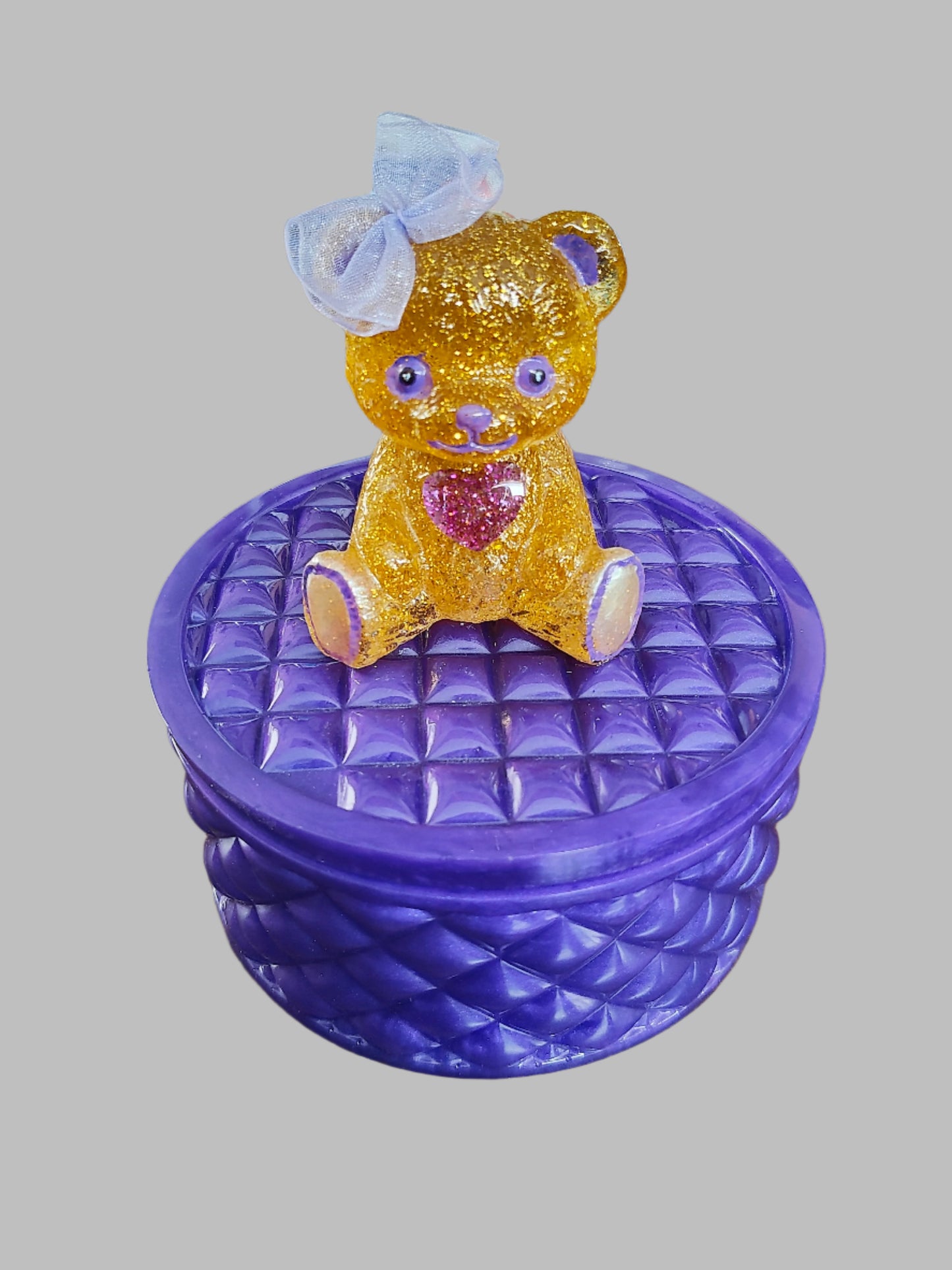 This adorable hand-crafted resin trinket box brings a touch of whimsy to your space! Featuring a charming teddy bear perched on top, it's the perfect home for jewelry, keepsakes, or small treasures. Measuring 5" x 5" x 5" with a 2" deep dish, this compact beauty combines functionality with personality. Crafted from smooth, durable epoxy resin that feels like glass, it's built to last while adding a playful accent to any dresser or shelf. At just 13 oz, it's lightweight enough to move around but sturdy enoug