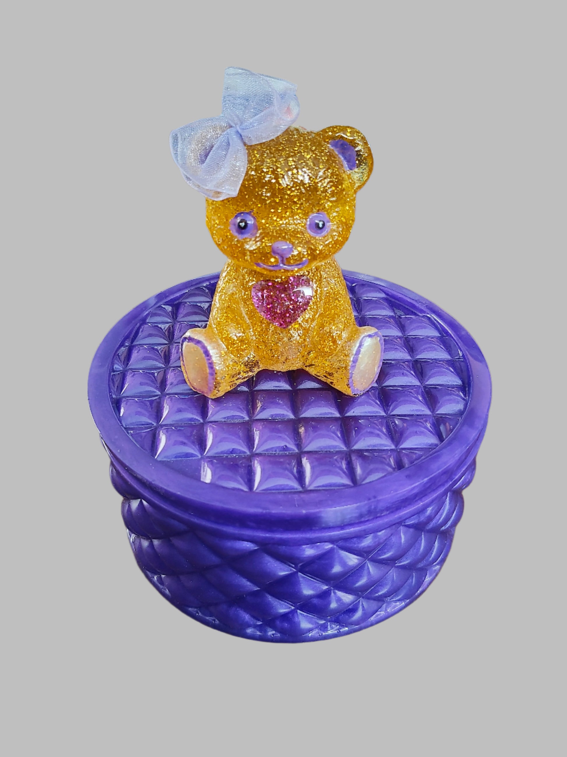 This adorable hand-crafted resin trinket box brings a touch of whimsy to your space! Featuring a charming teddy bear perched on top, it's the perfect home for jewelry, keepsakes, or small treasures. Measuring 5" x 5" x 5" with a 2" deep dish, this compact beauty combines functionality with personality. Crafted from smooth, durable epoxy resin that feels like glass, it's built to last while adding a playful accent to any dresser or shelf. At just 13 oz, it's lightweight enough to move around but sturdy enoug