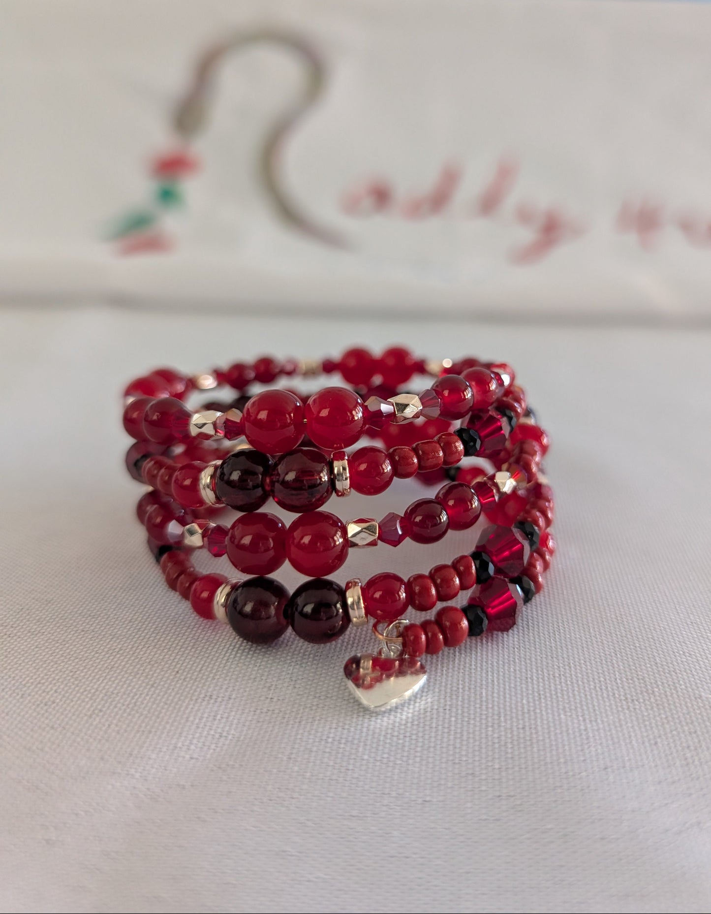 Elevate your everyday style with this stunning red memory wire bracelet, designed to make a lasting impression. Featuring a captivating mix of 8mm, 6mm, and 4mm red glass and crystal beads that catch the light beautifully, this piece combines elegance with versatility. Delicate gold spacer beads and vibrant red seed beads add intricate detail, while a charming silver heart pendant serves as the perfect finishing touch. The four-coil memory wire construction ensures a comfortable, secure fit that adapts to y