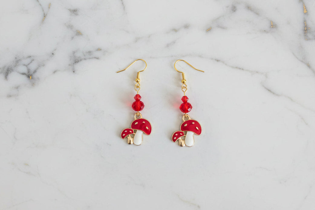 Enchanting mushroom earrings featuring delicate crystal beads nestled on lustrous gold plated hooks. Each earring measures approximately 2 inches, striking the perfect balance between statement-making and wearable elegance. At just 0.15 oz per pair, these lightweight beauties won't weigh you down, making them ideal for all-day wear. The shimmering gold plating catches the light beautifully, while the crystal accents add a touch of sparkle and sophistication. 
