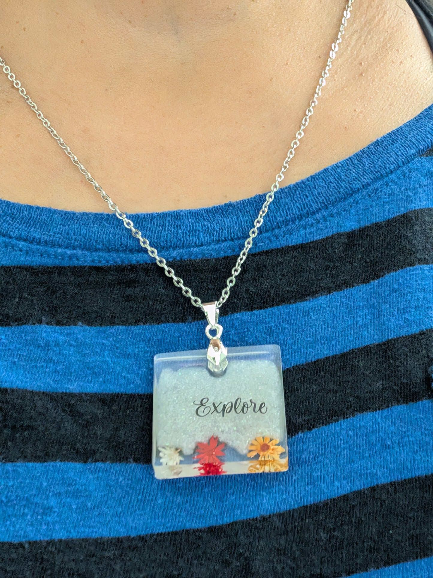 This stainless steel cable link chain necklace features a beautiful square pendant with real flowers embedded in resin. The necklace is 21 inches long, with an additional 2 inch extension chain. Make a statement with this one-of-a-kind piece!

Necklace - 21 inches stainless steel cable link chain with a resin with flowers square pendant