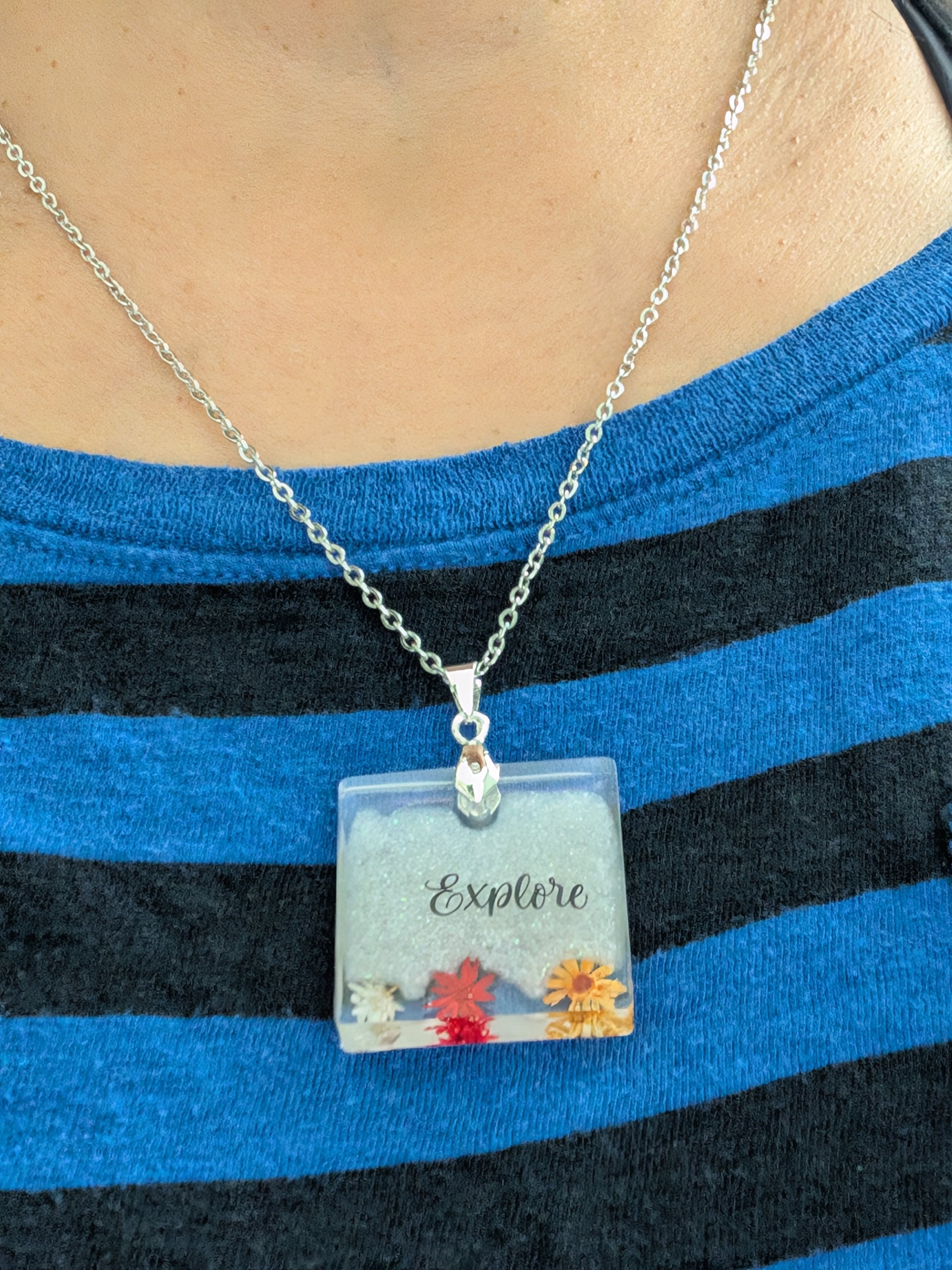 This stainless steel cable link chain necklace features a beautiful square pendant with real flowers embedded in resin. The necklace is 21 inches long, with an additional 2 inch extension chain. Make a statement with this one-of-a-kind piece!

Necklace - 21 inches stainless steel cable link chain with a resin with flowers square pendant