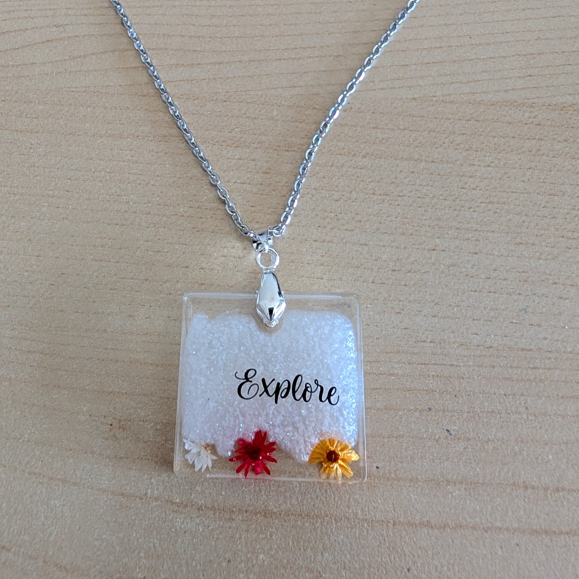This stainless steel cable link chain necklace features a beautiful square pendant with real flowers embedded in resin. The necklace is 21 inches long, with an additional 2 inch extension chain. Make a statement with this one-of-a-kind piece!

Necklace - 21 inches stainless steel cable link chain with a resin with flowers square pendant