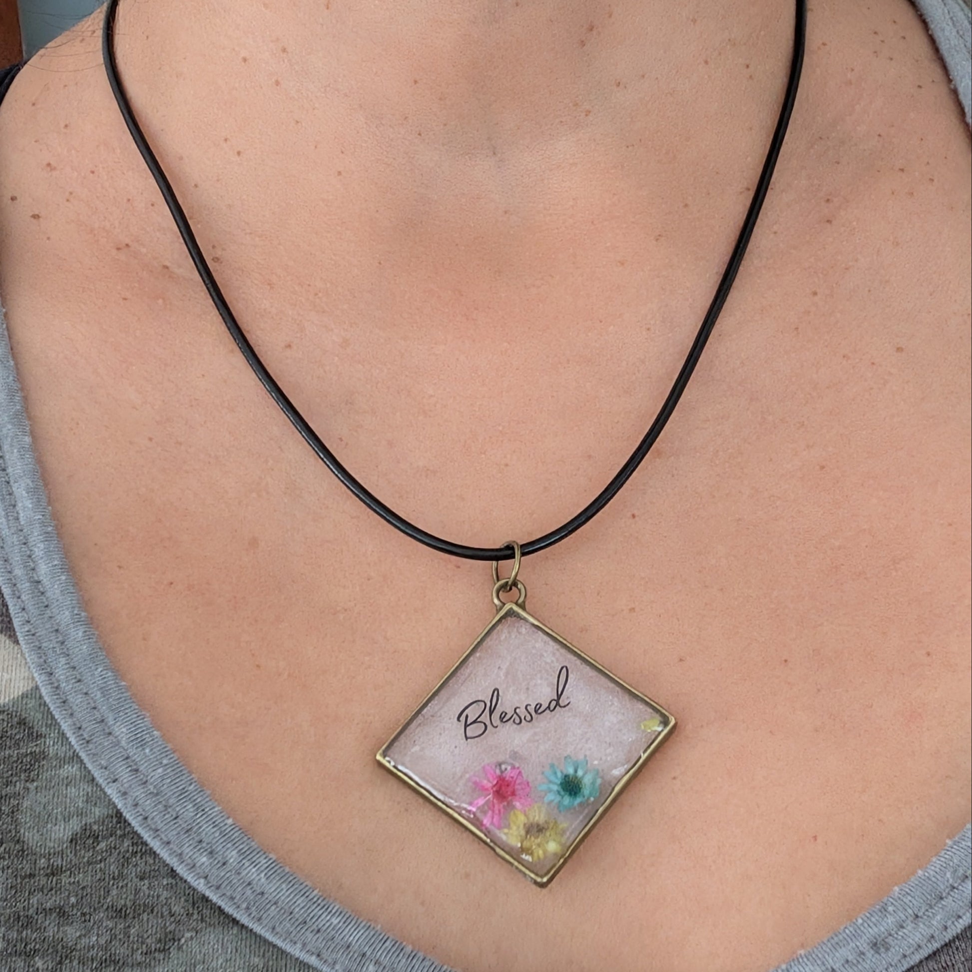 Elevate any outfit with our stunning 18 inches resin and flowers bronze diamond pendant necklace. The intricate Blessed design adds a touch of elegance, while the black 2mm leather cord provides a bold contrast. Lightweight and versatile, perfect for any occasion.