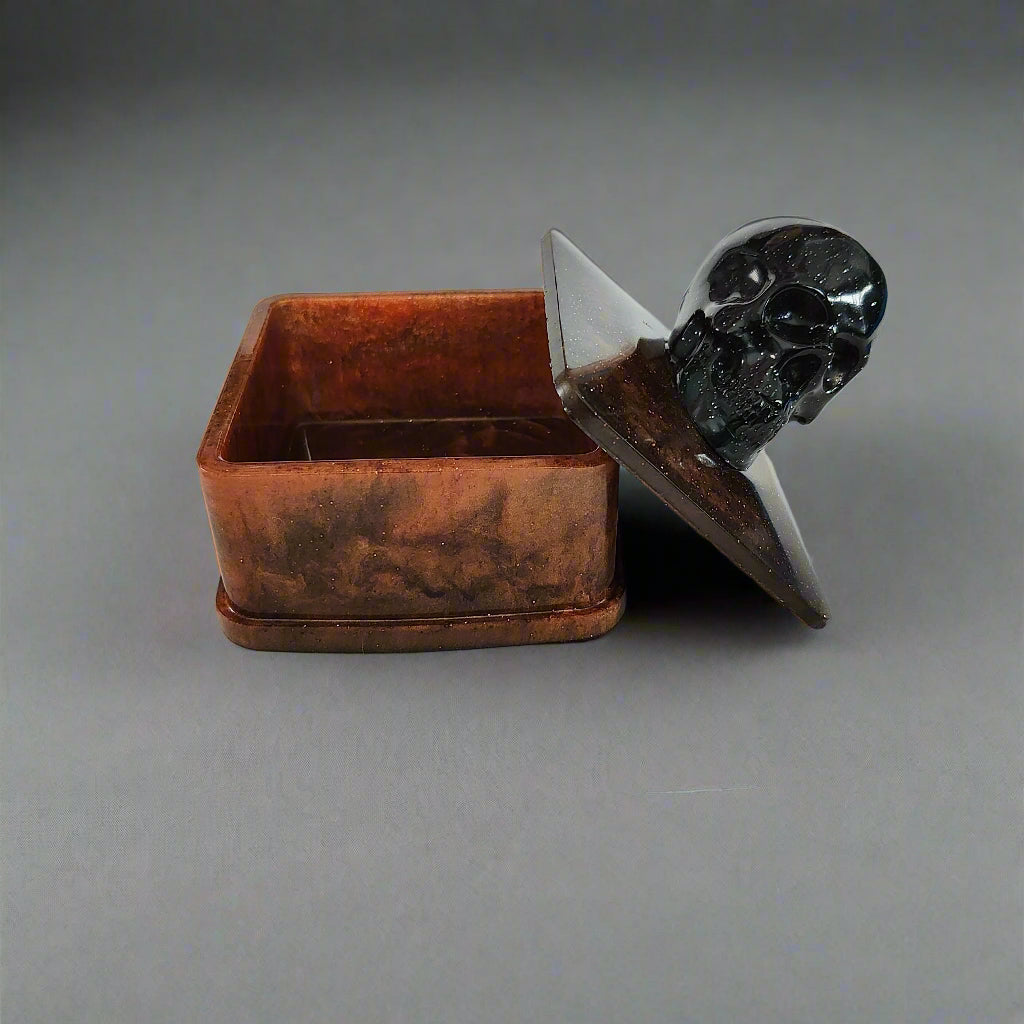 Say goodbye to boring trinket boxes and hello to this quirky Knickknack! Made of sturdy resin, it features a skull lid that adds a touch of spookiness to your decor. With dimensions of 3 x 3 x 3.5 inches and weighing only 5 oz, it's perfect for storing your knickknacks in style.

Resin square jewelry/trinket box with skull lid