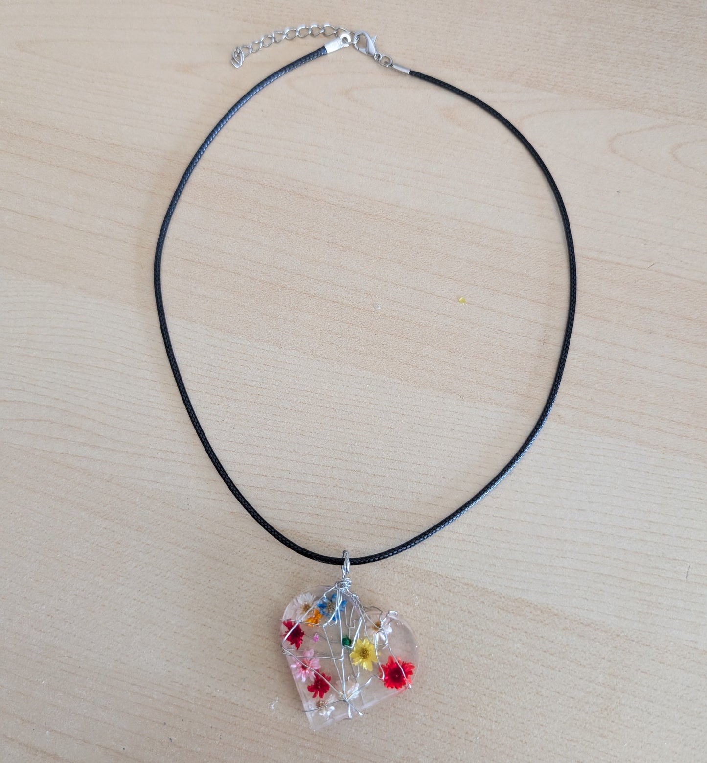 This stunning necklace features a heart-shaped pendant made of clear resin and real dried flowers, delicately suspended on a black cord. Measuring at 17.5 inches (plus a 2-inch extension chain), this unique piece adds a touch of nature and charm to any outfit.

Necklace - 17.5 inches clear resin with dried flowers heart on black cord