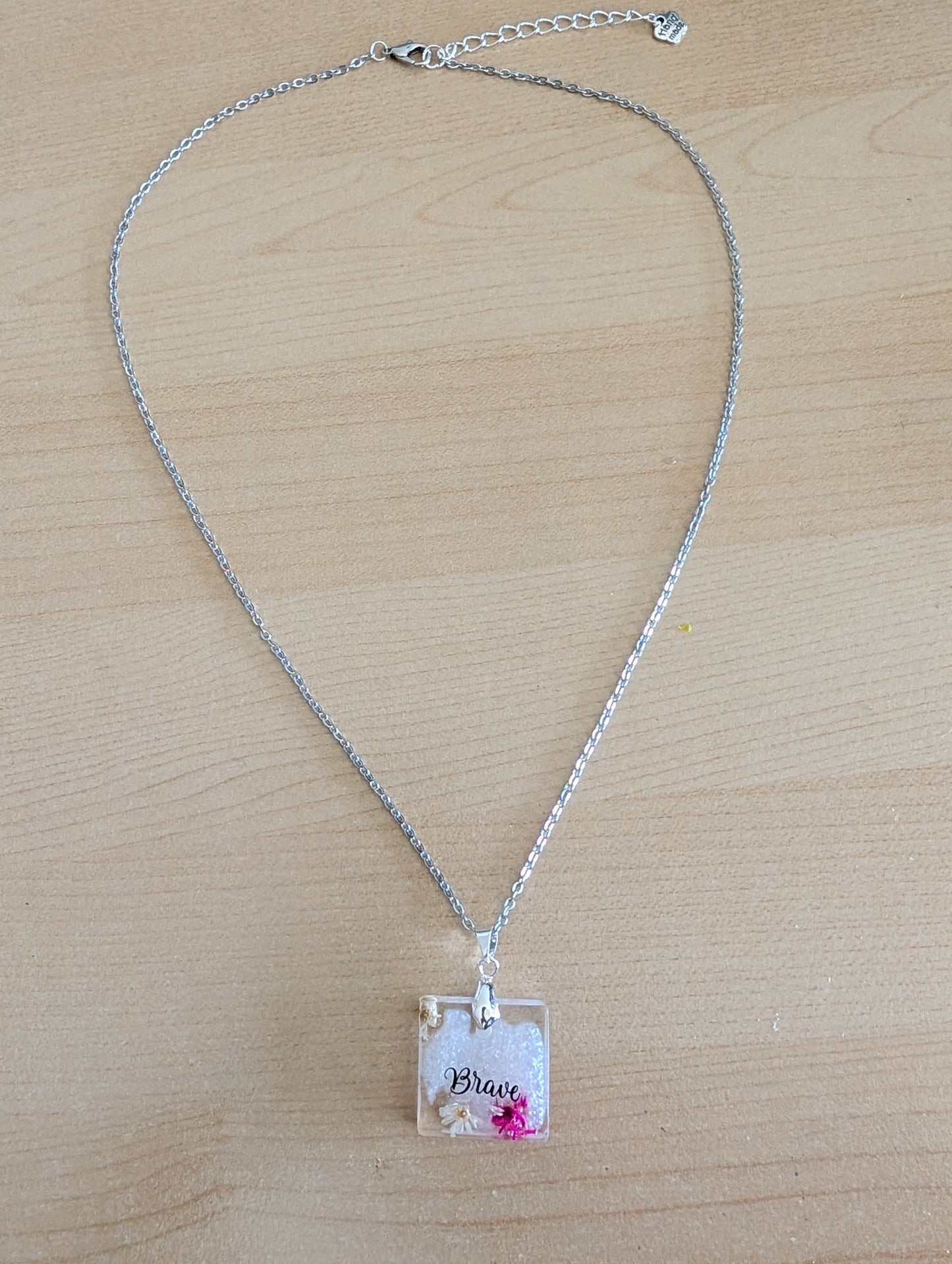 This stainless steel cable link chain necklace features a beautiful square pendant with real flowers embedded in resin. The necklace is 21 inches long, with an additional 2 inch extension chain. Make a statement with this one-of-a-kind piece!

Necklace - 21 inches stainless steel cable link chain with a resin with flowers square pendant