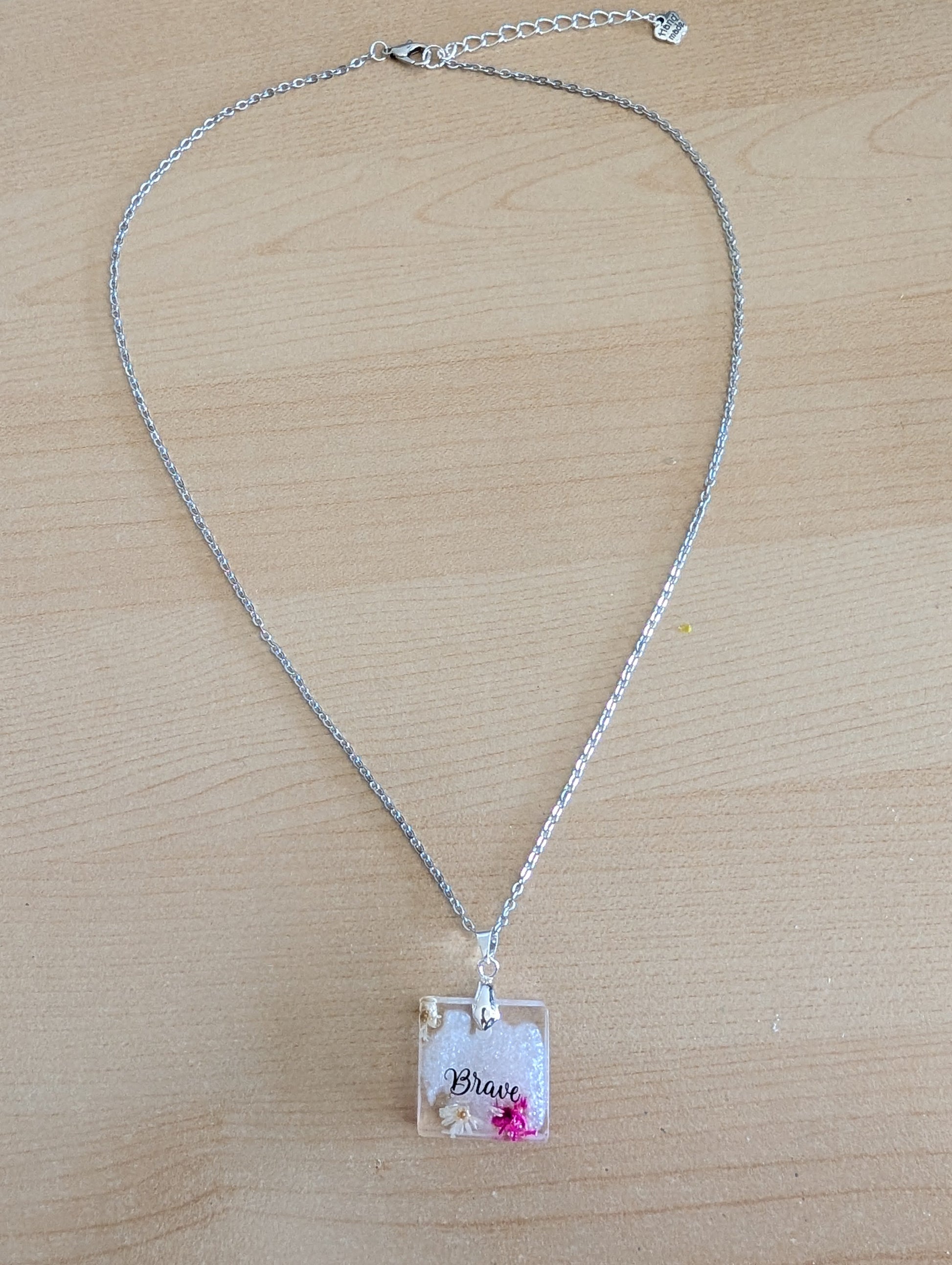 This stainless steel cable link chain necklace features a beautiful square pendant with real flowers embedded in resin. The necklace is 21 inches long, with an additional 2 inch extension chain. Make a statement with this one-of-a-kind piece!

Necklace - 21 inches stainless steel cable link chain with a resin with flowers square pendant
