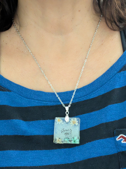 This stainless steel cable link chain necklace features a beautiful square pendant with real flowers embedded in resin. The necklace is 21 inches long, with an additional 2 inch extension chain. Make a statement with this one-of-a-kind piece!

Necklace - 21 inches stainless steel cable link chain with a resin with flowers square pendant