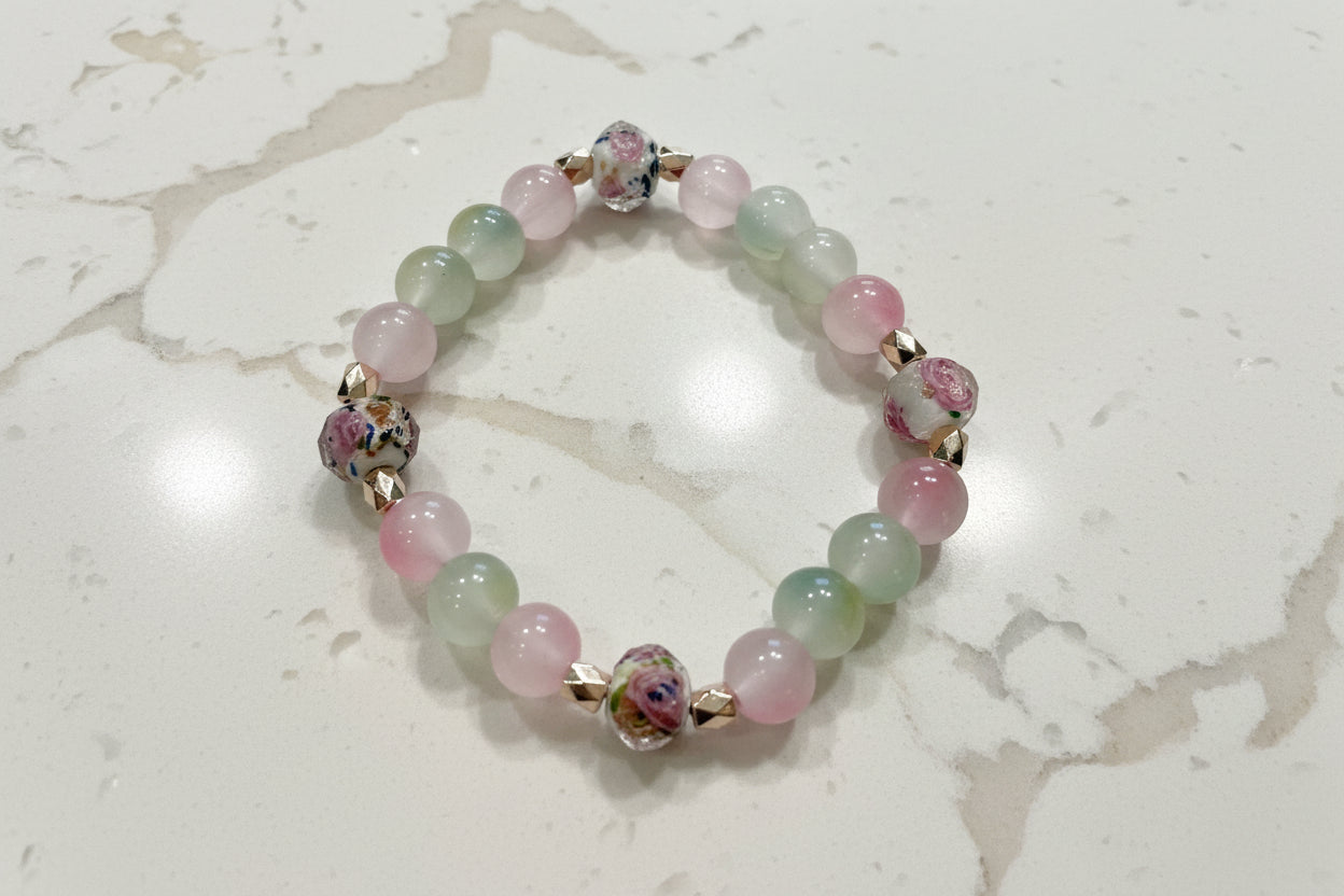 This stunning Bracelet features 9mm rose gold sand lampwork beads, complemented by 8mm pink and green glass beads. Adorned with gold rose spacer beads, the elastic design ensures a comfortable and secure fit. Elevate your style with this beautifully crafted piece.