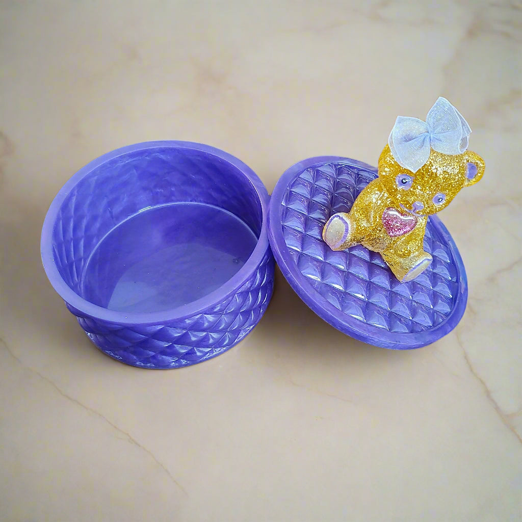 This adorable hand-crafted resin trinket box brings a touch of whimsy to your space! Featuring a charming teddy bear perched on top, it's the perfect home for jewelry, keepsakes, or small treasures. Measuring 5" x 5" x 5" with a 2" deep dish, this compact beauty combines functionality with personality. Crafted from smooth, durable epoxy resin that feels like glass, it's built to last while adding a playful accent to any dresser or shelf. At just 13 oz, it's lightweight enough to move around but sturdy enoug