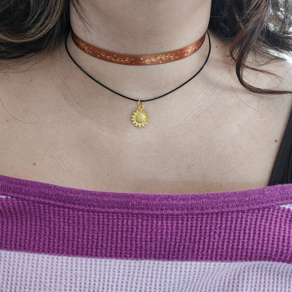 This elegant necklace features a fall-themed design with satin metallic leaves and a gold charm, all on a sleek choker ribbon. The combination of satin and metal creates a beautiful contrast, while the polyester strand adds durability. Perfect for adding a touch of sophistication to any outfit!