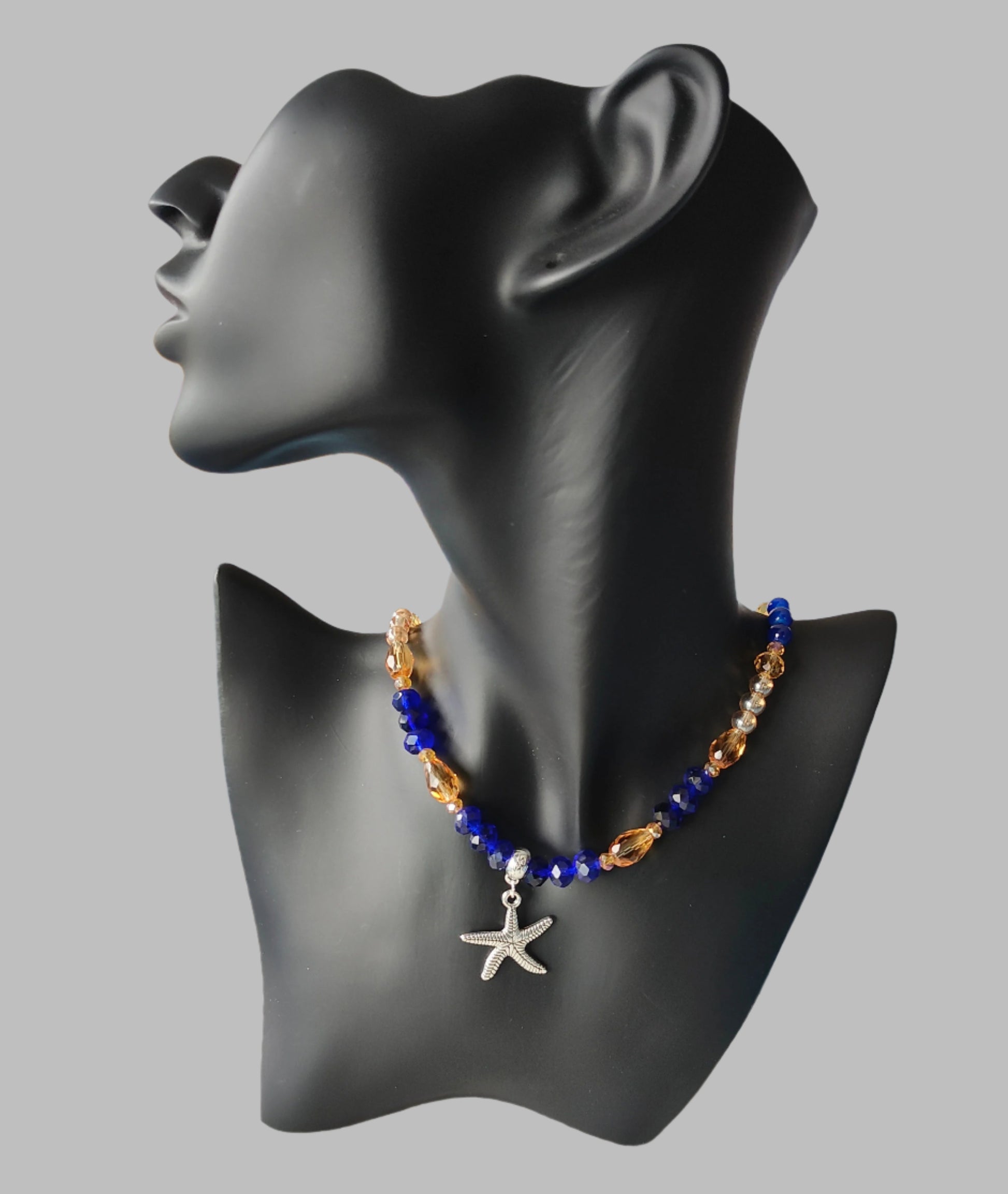 Add a touch of the ocean to your outfit with our Silver Starfish Necklace. Featuring a delicate silver starfish charm adorned with blue and gold crystal and glass beads, this necklace is perfect for any occasion. Choose between 16 and 18 inches for the perfect fit, and enjoy its lightweight design at only 0.72 oz.

Necklace - Silver starfish charm with blue and gold crystal and glass beads