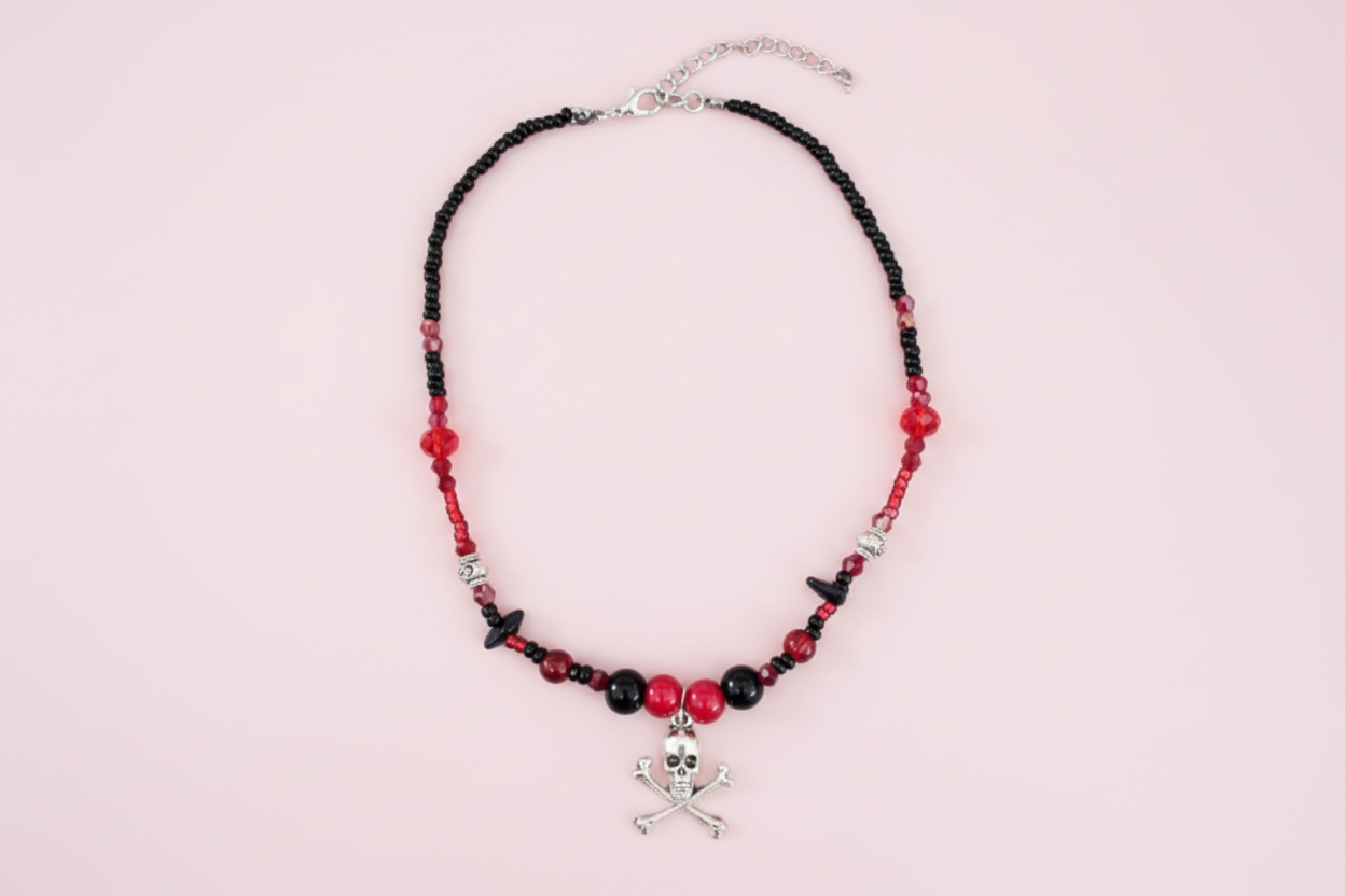 Necklace with black and red beads and a skull charm on a pink background