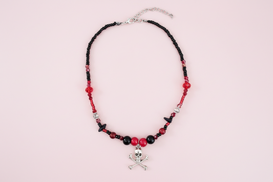 Necklace with black and red beads and a skull charm on a pink background